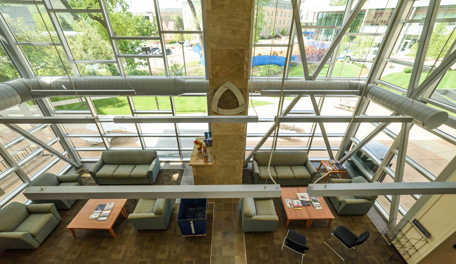 Interior with high glass walls and seating in a lobby, mines logo on wall, outside green grass and ttrees